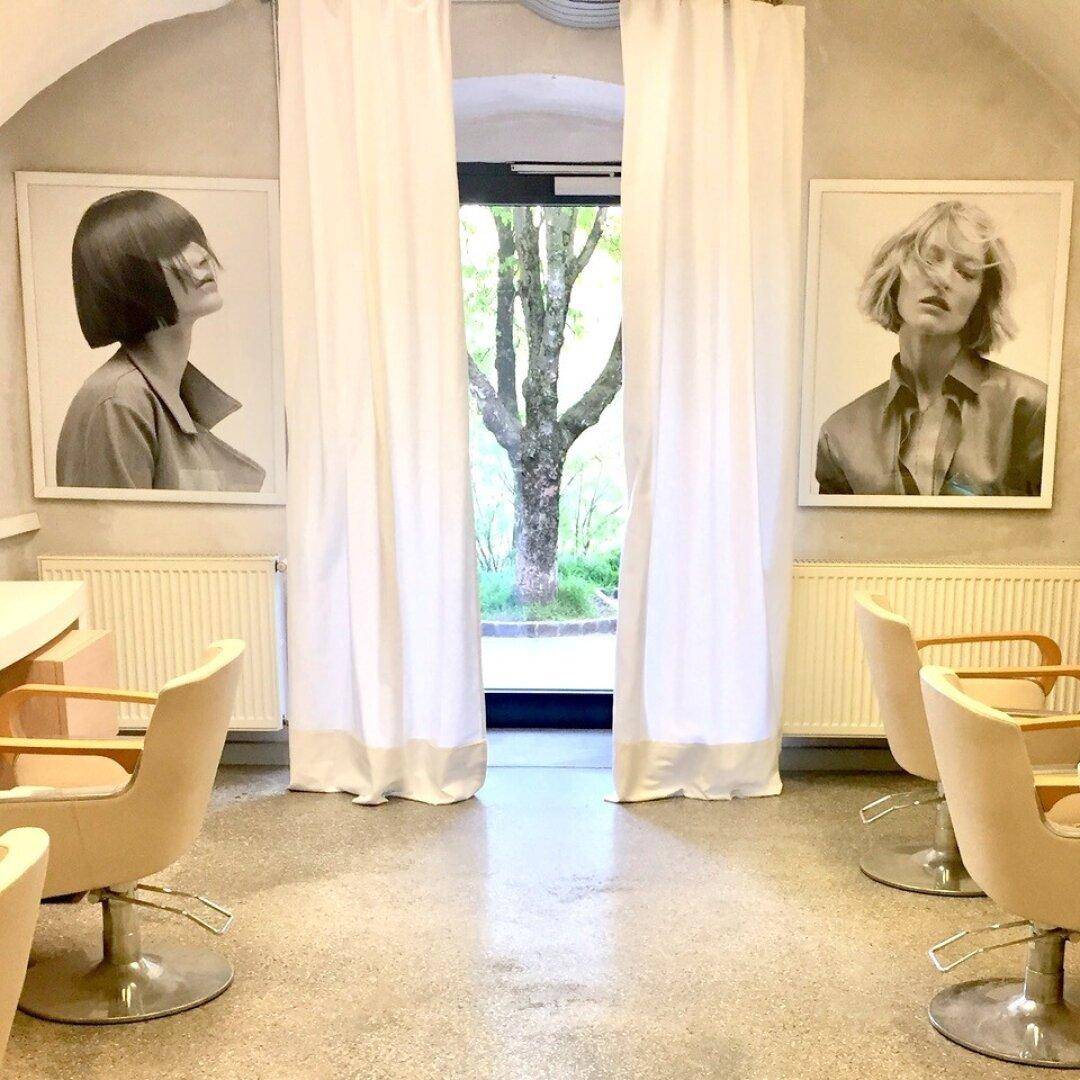 Moderner Salonbereich mit großen Fenstern, Stylingstühlen und hellem Betonboden.