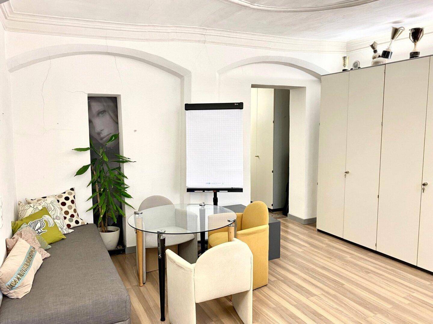 Büro- oder Besprechungsraum mit gewölbter Decke, kleinem Tisch und Einbauschränken.