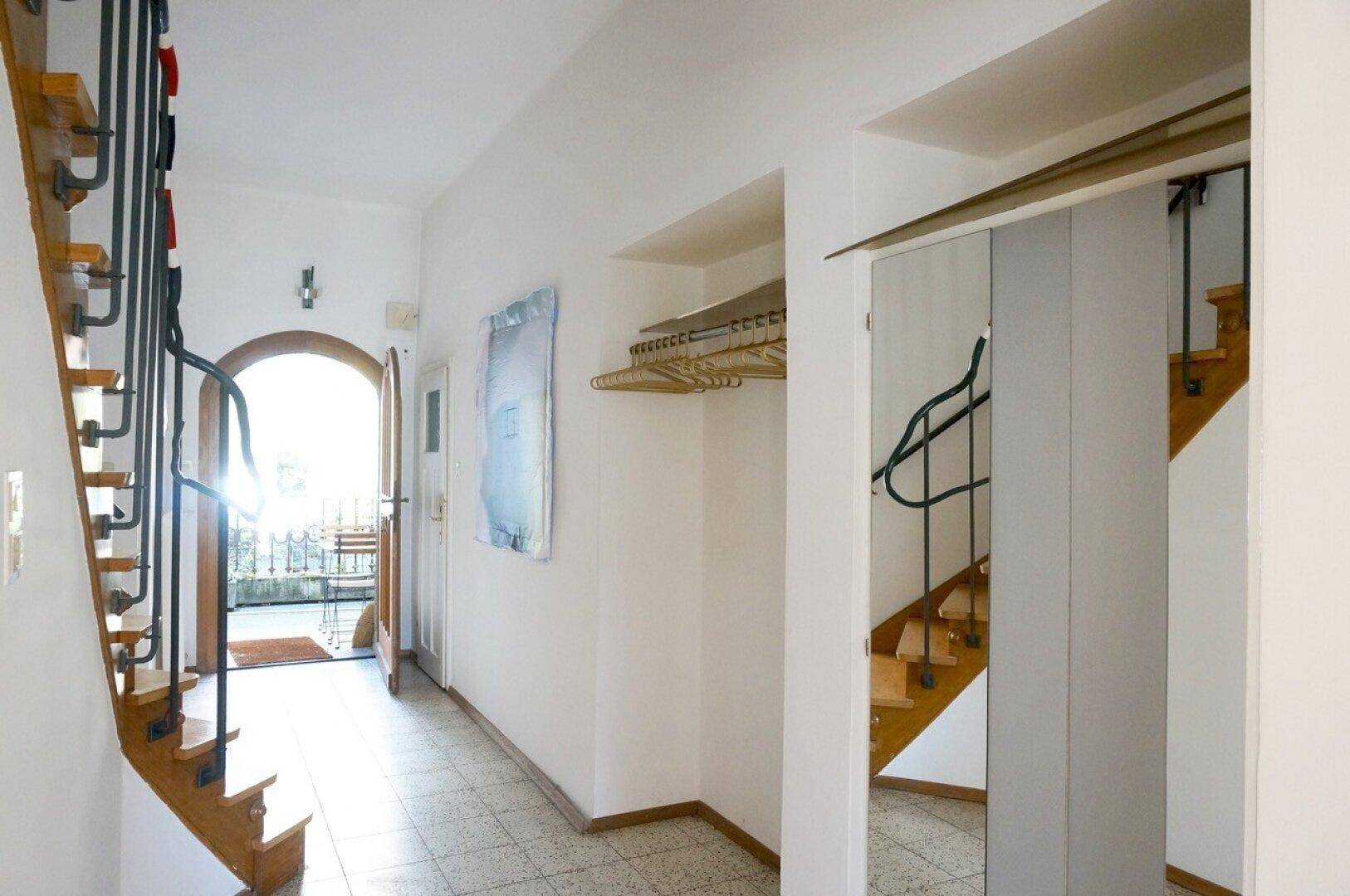 Heller Flur mit gefliestem Boden, Treppe und Zugang zu einem Außenbereich.