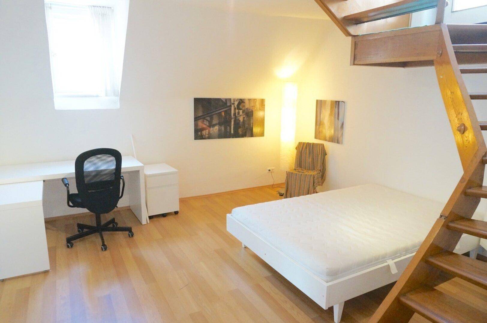 Schlafzimmer mit Holzboden, Schreibtisch und einer offenen Holztreppe.