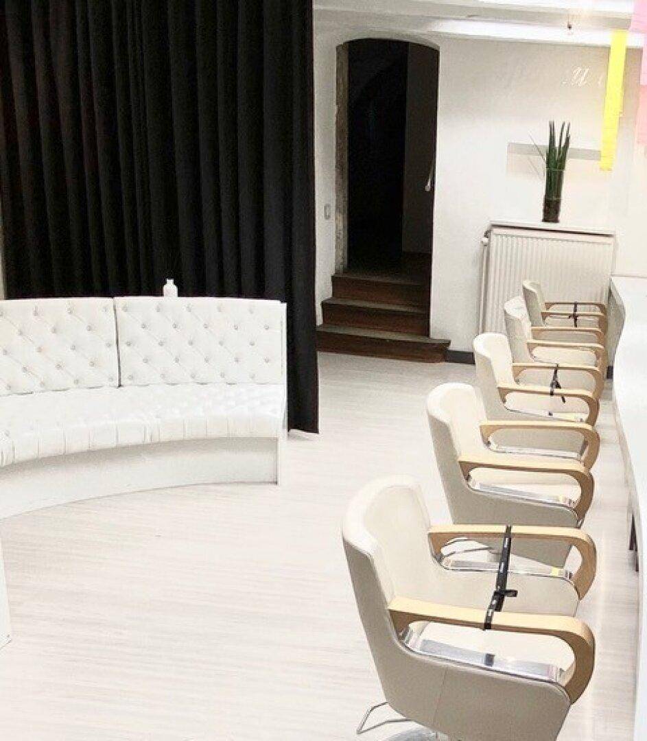 Wartebereich eines Friseursalons mit weißem Sofa und hellen Stylingstühlen.