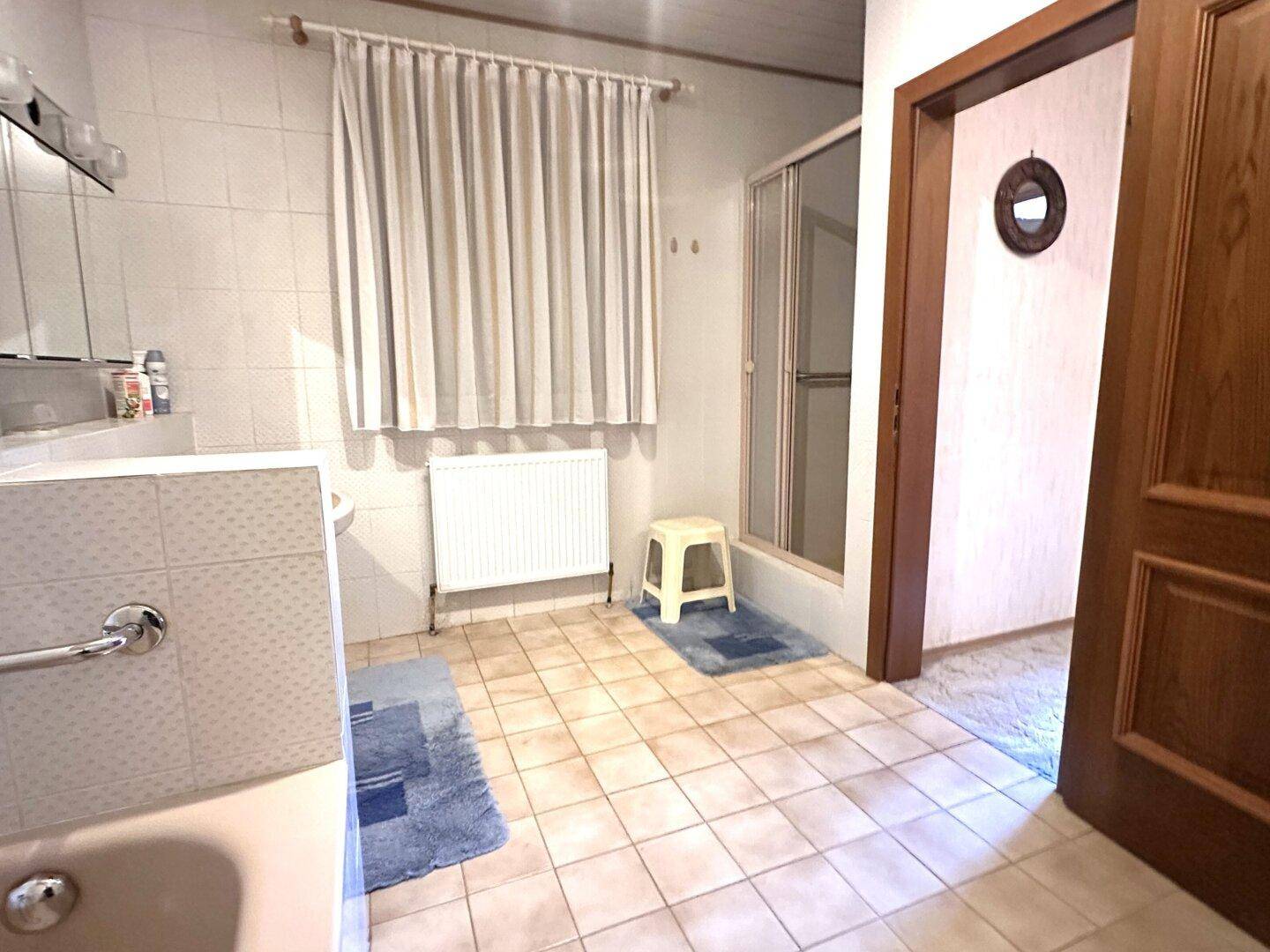 Älteres Badezimmer mit Duschkabine, Heizkörper und Fenster, ausgestattet mit Fliesenboden.