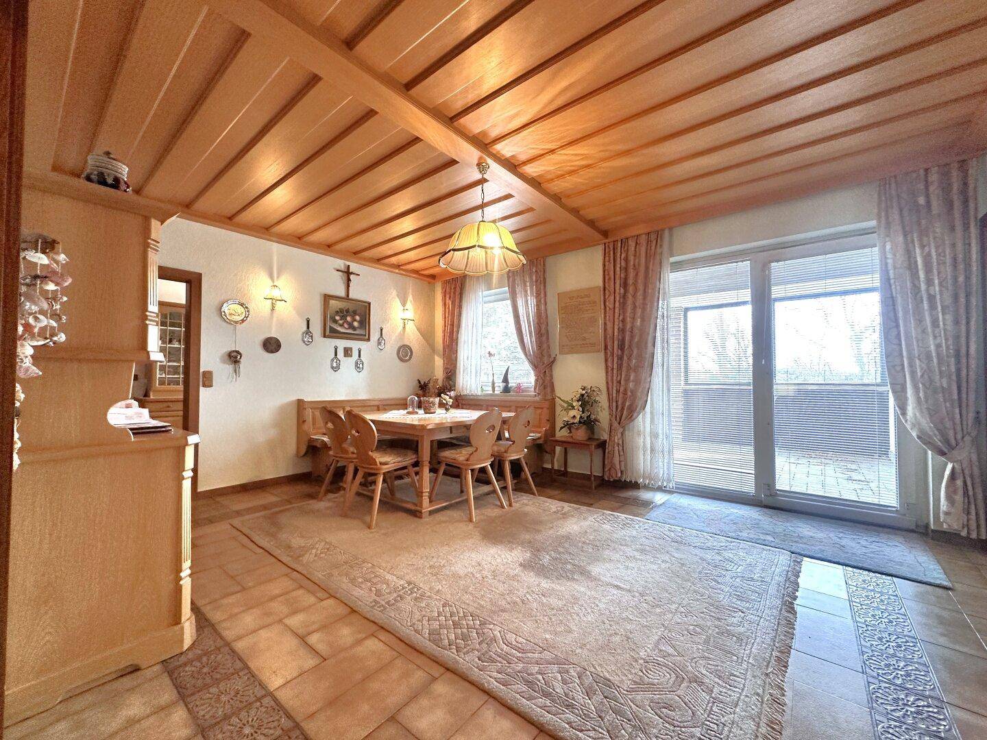 Traditioneller Essbereich mit Holztisch, Eckbank und Zugang zur Terrasse, umgeben von warmen Holzelementen.