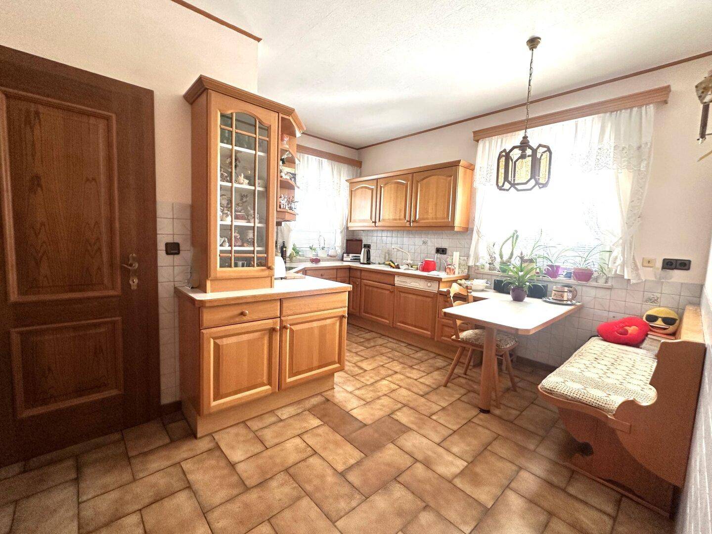 Rustikale Küche mit Holzschränken, Fliesenboden und gemütlichem Essbereich am Fenster.