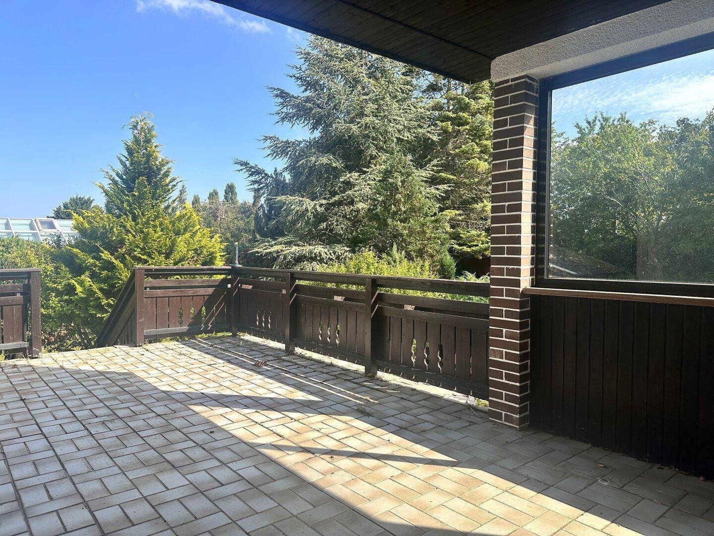 Geräumige, geflieste Terrasse mit Holzgeländer und viel Platz für individuelle Gestaltung.