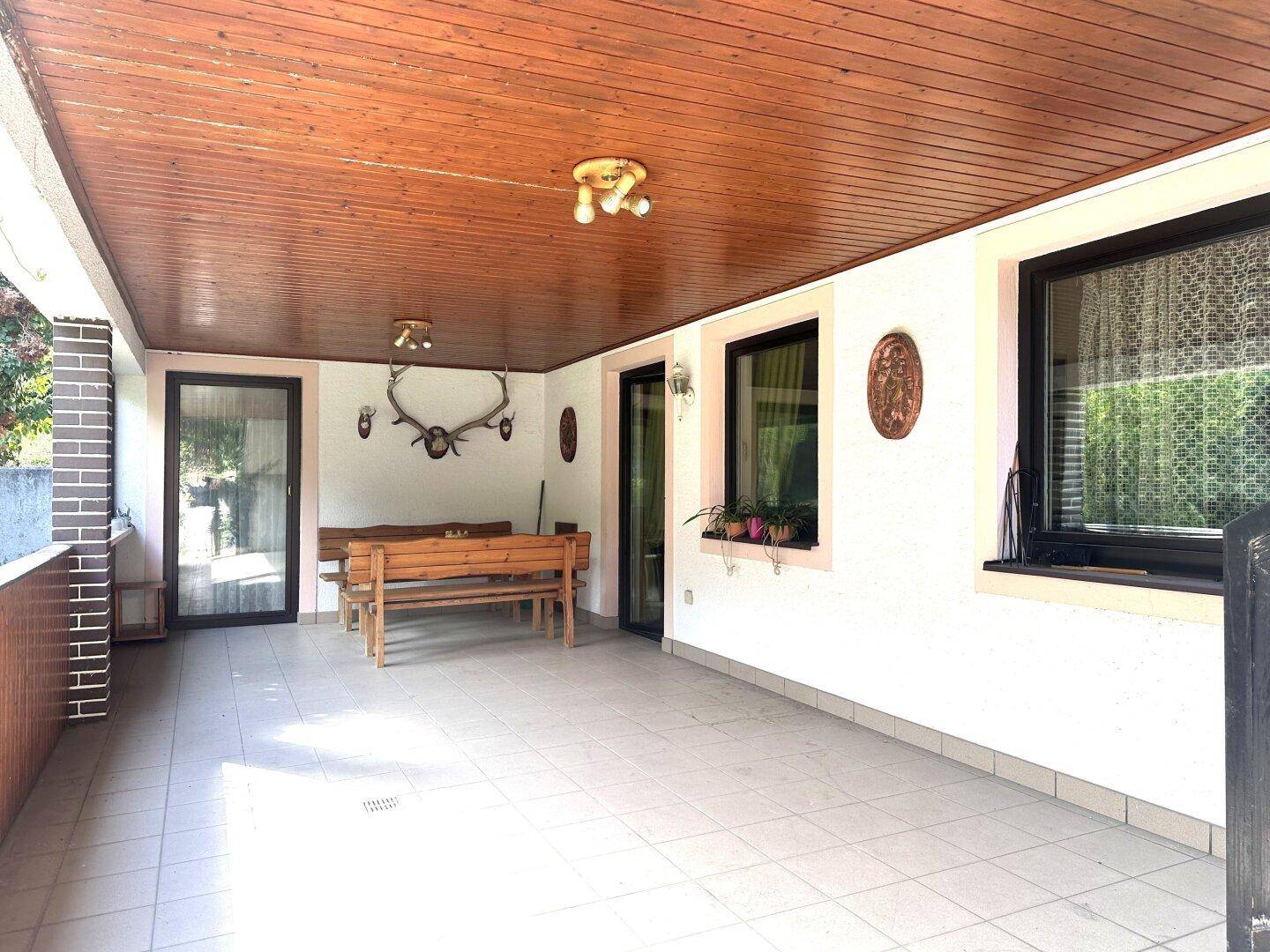 Überdachte Terrasse mit Holzbalkendecke, traditionellen Sitzbänken und Geweih-Dekoration.