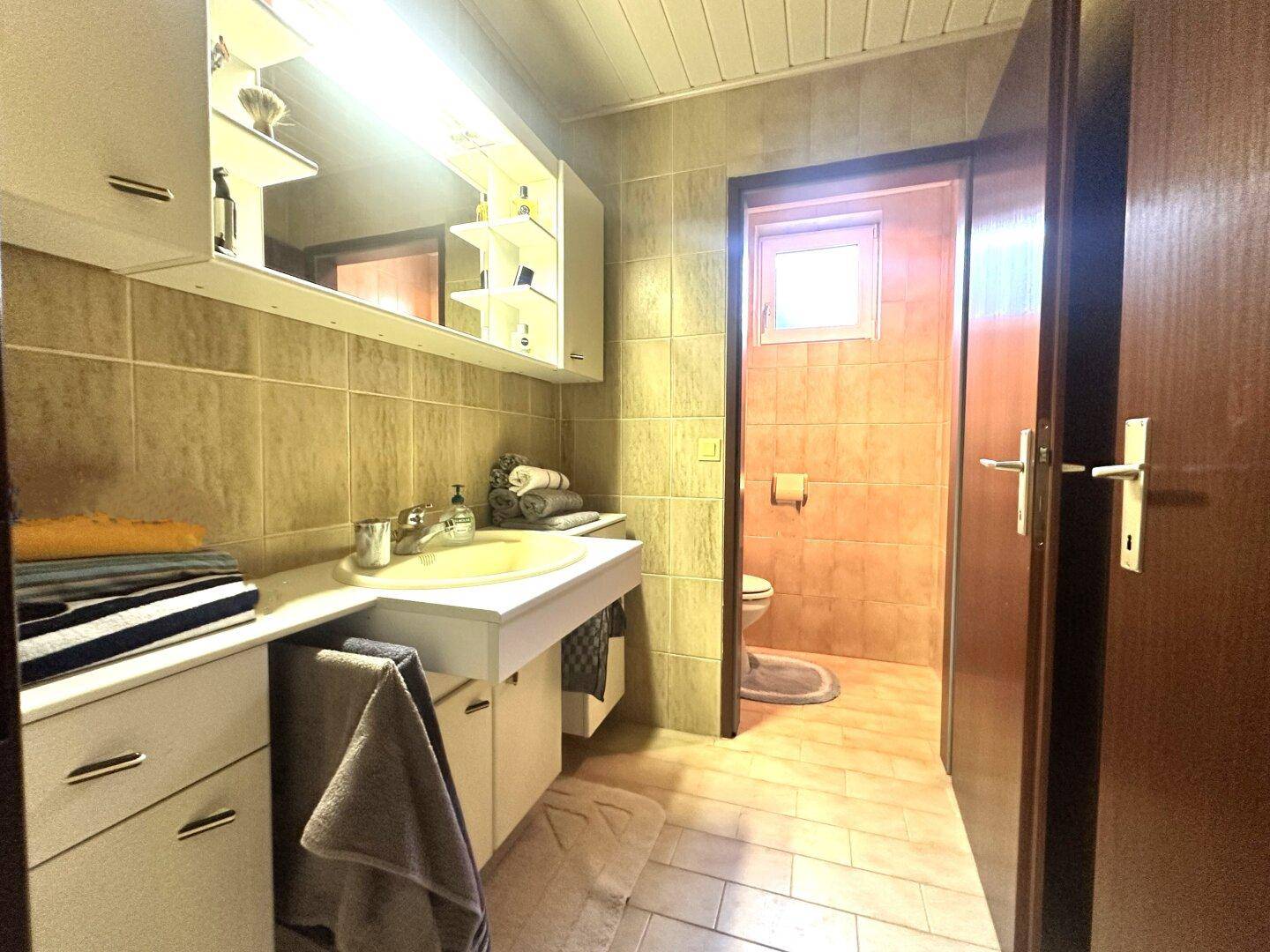 Kleines Badezimmer im Untergeschoss mit Waschbecken, Spiegelschrank und Fliesen an Wänden und Boden.