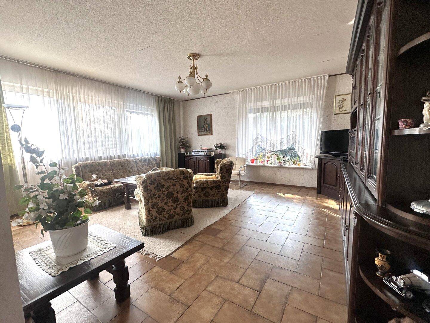 Geräumiges Wohnzimmer im klassischen Stil mit Fliesenboden, großen Fenstern und traditionellen Möbeln.