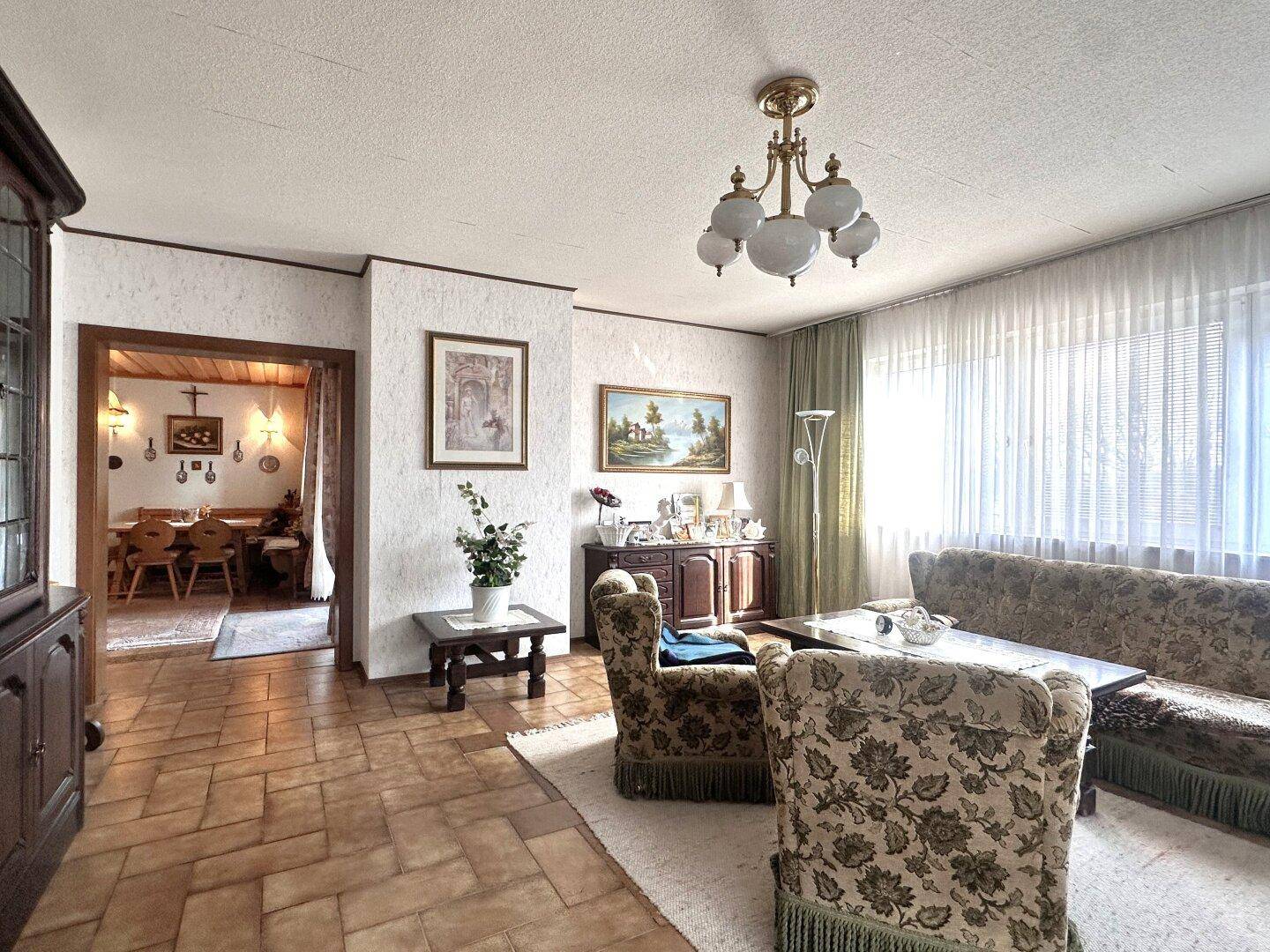 Traditionelles Wohnzimmer mit bequemen Sesseln, Fliesenboden und Blick in den angrenzenden Essbereich.