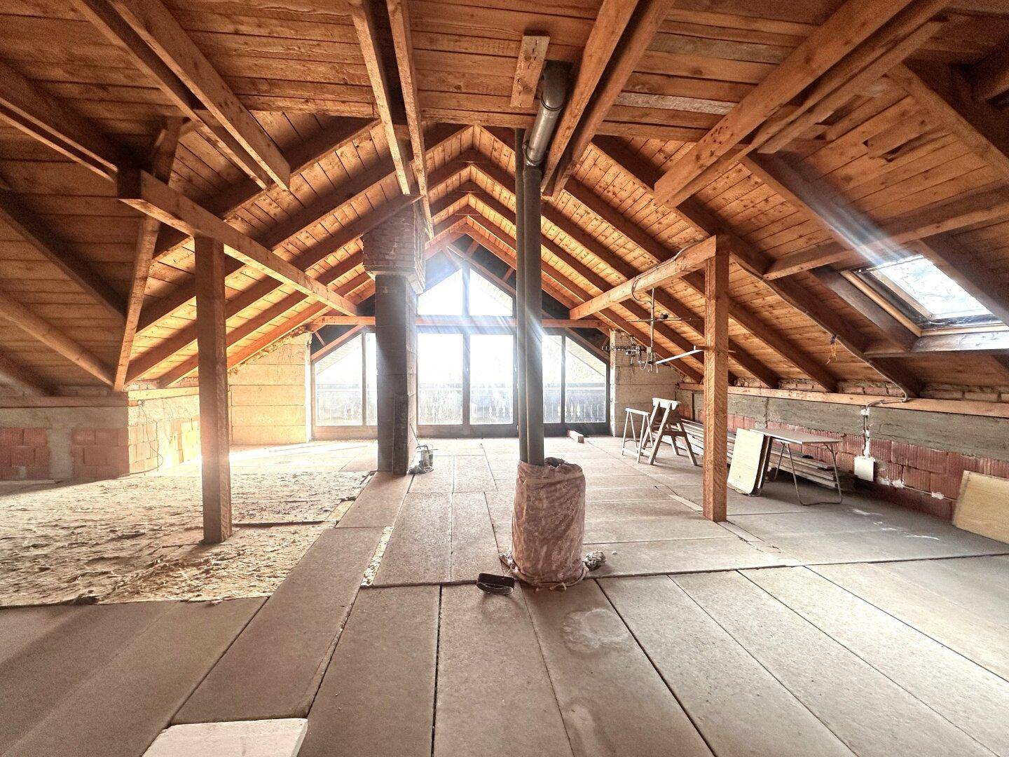 Unausgebautes Dachgeschoss mit sichtbaren Holzbalken und Dachfenstern, bereit für den Ausbau.