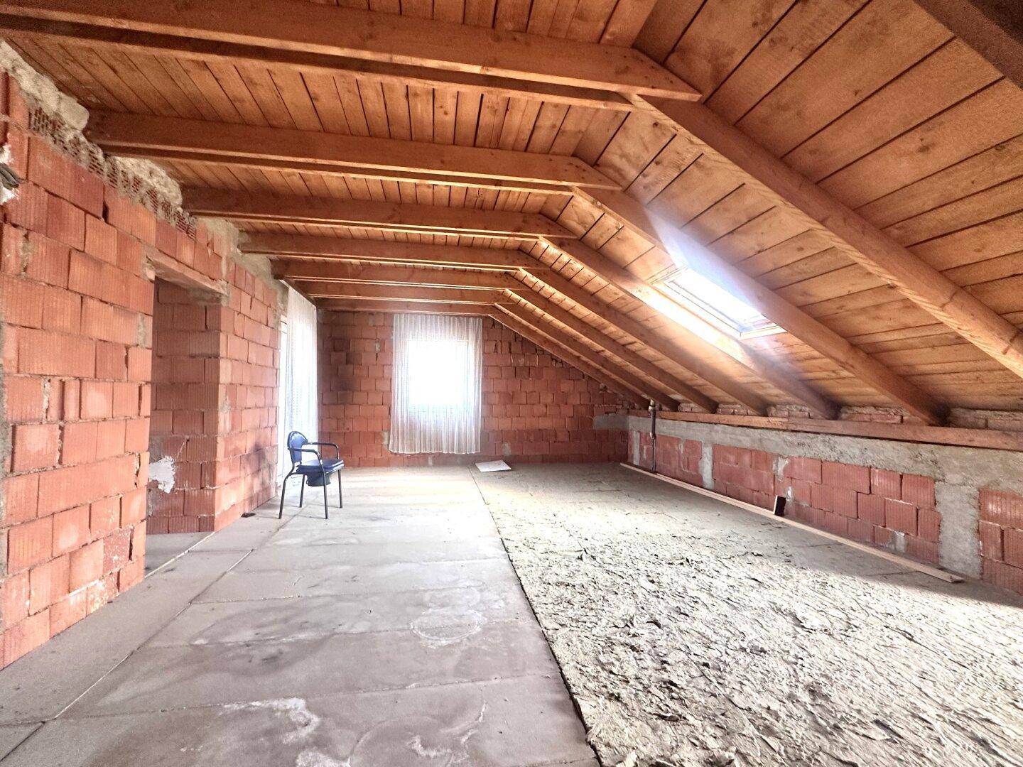 Geräumiges Dachgeschoss im Rohbau mit sichtbaren Holzbalken und einem Fenster.