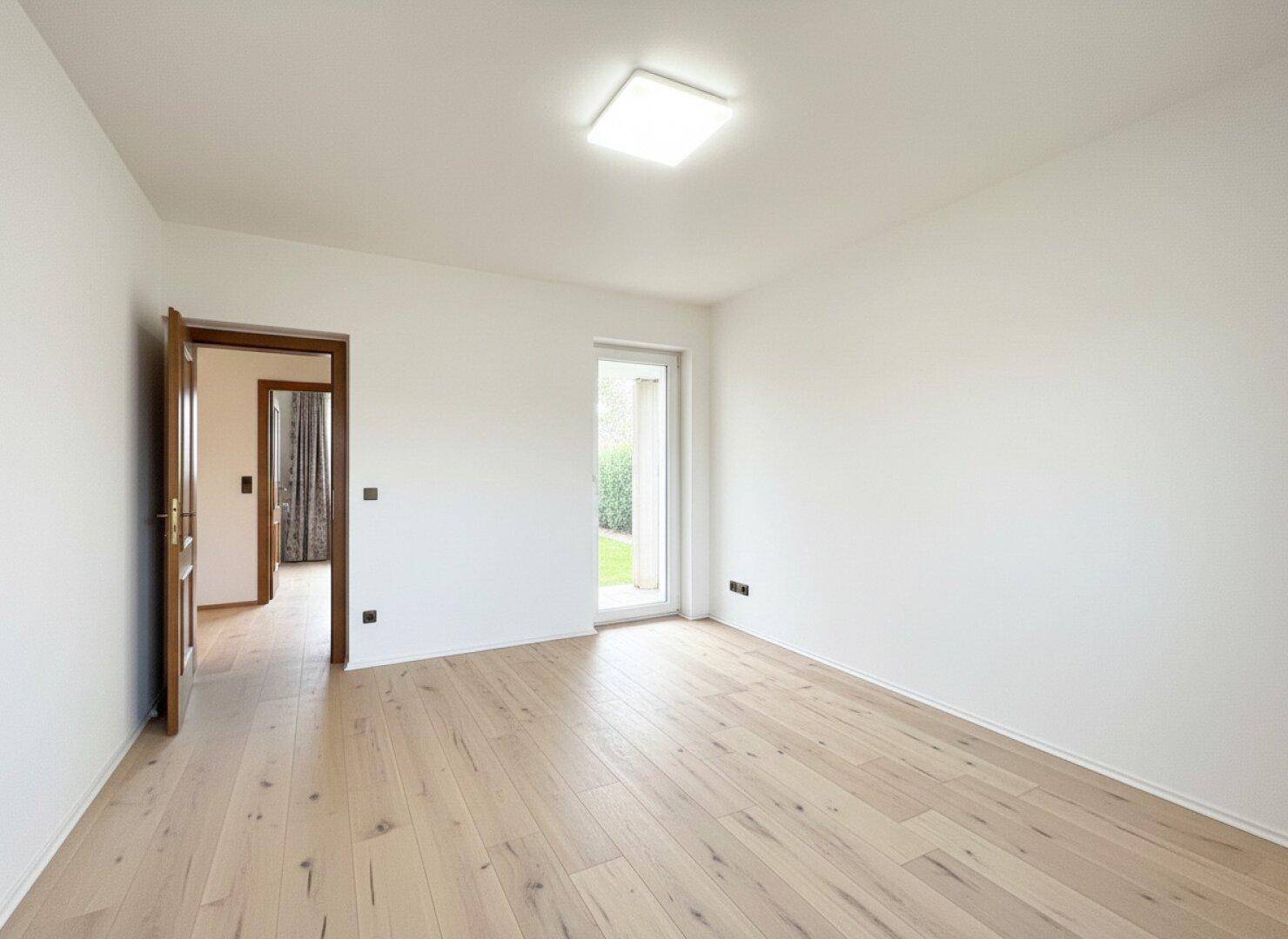 Helles, leeres Zimmer mit Holzboden und direktem Zugang zum Garten, ideal als Schlafzimmer.