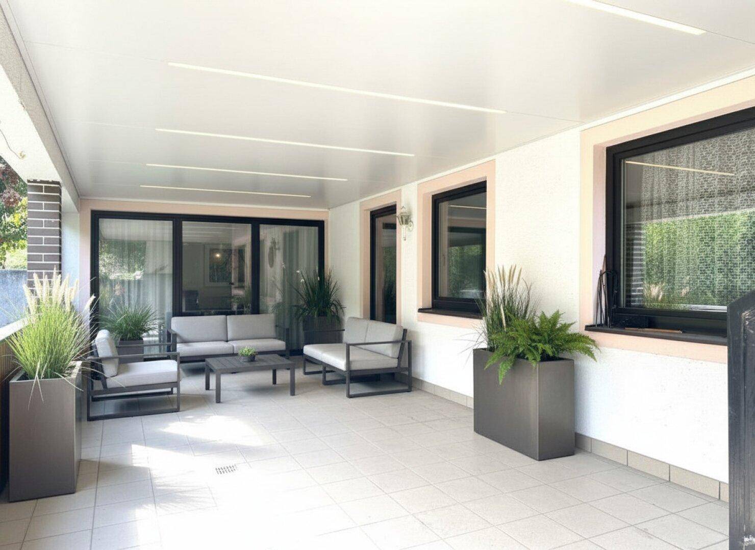 Überdachte Terrasse mit modernen Lounge-Möbeln und Pflanzen, ideal für entspannte Stunden im Freien.