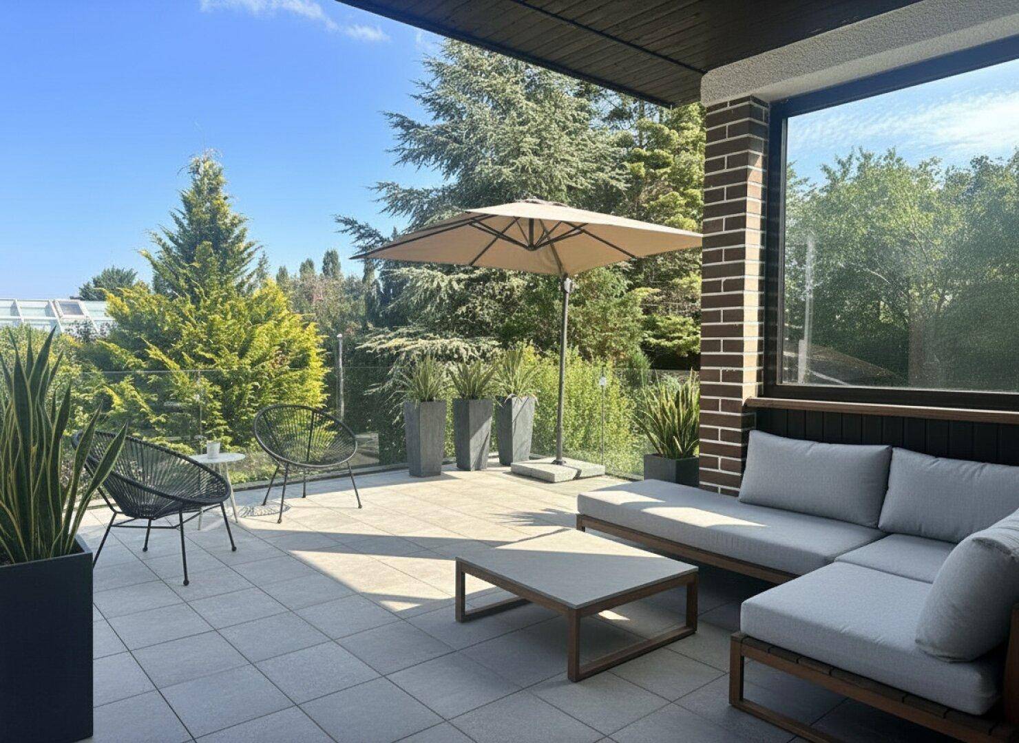 Moderne, möblierte Terrasse mit Lounge-Möbeln, Sonnenschirm und Blick ins Grüne.