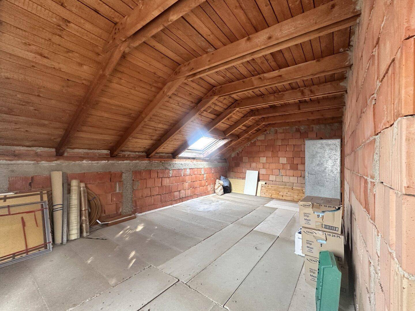 Dachgeschoss im Rohzustand mit Holzbalken und Dachfenster, ideal für zusätzlichen Wohnraum.