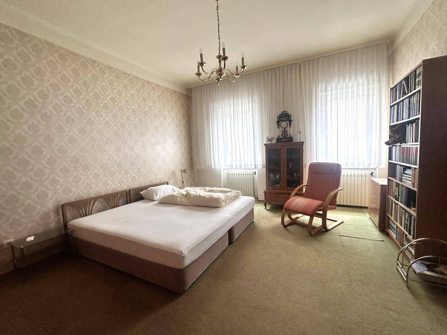 Geräumiges Schlafzimmer mit Teppichboden, gemusterter Tapete und traditionellen Möbeln.