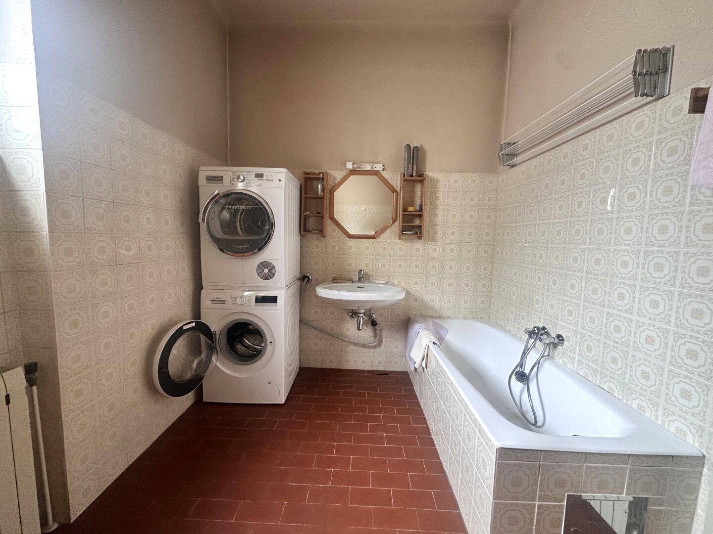 Älteres Badezimmer mit Badewanne, Waschmaschine und gemusterten Fliesen.
