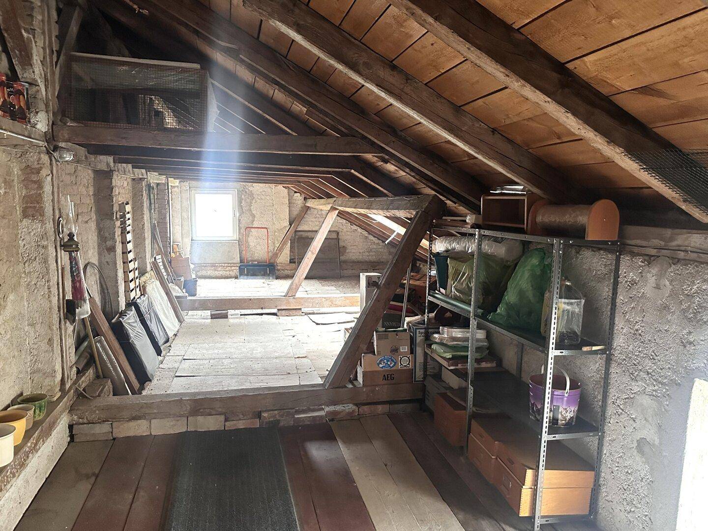 Unausgebauter Dachbodenbereich mit Lagerregalen und sichtbarer Holzkonstruktion.