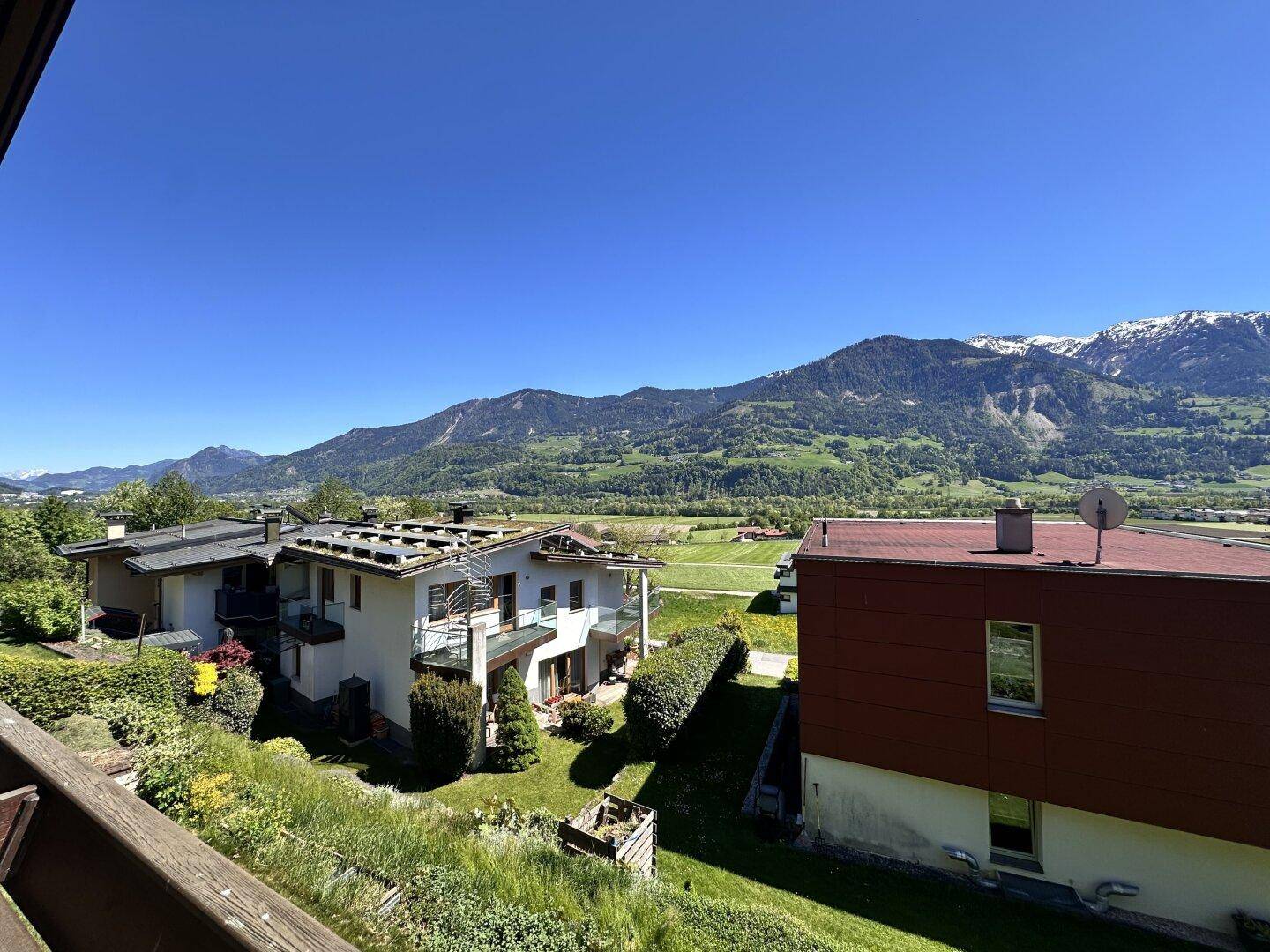 Weitläufiger Panoramablick über die grüne Landschaft mit Häusern und majestätischen Bergen im Hintergrund.