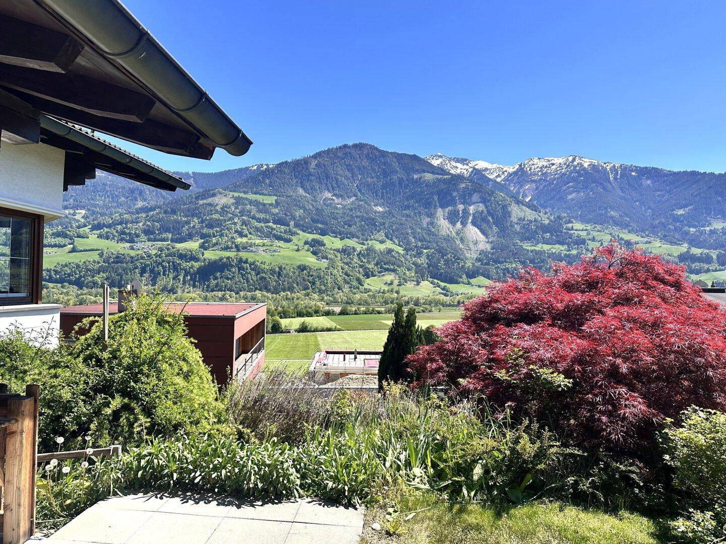 Malerischer Ausblick auf grüne Berge und schneebedeckte Gipfel von einem erhöhten Standpunkt.