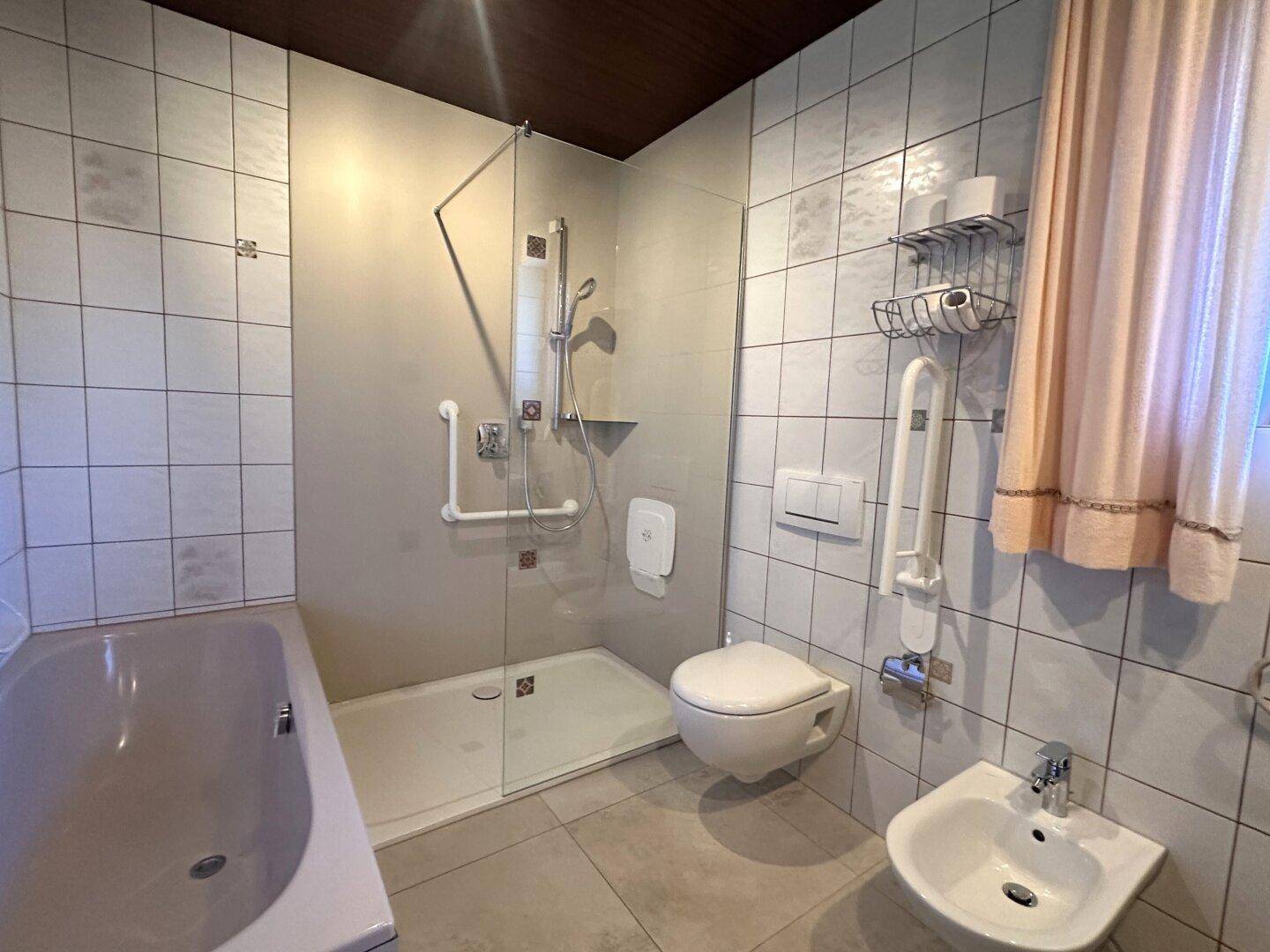 Geräumiges Badezimmer mit Badewanne, ebenerdiger Dusche, Toilette, Bidet und Fenster.