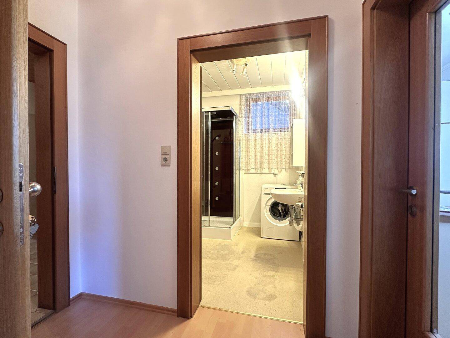 Hauswirtschaftsraum mit Waschmaschine, Waschbecken und Duschkabine, ausgestattet mit einem Fenster.