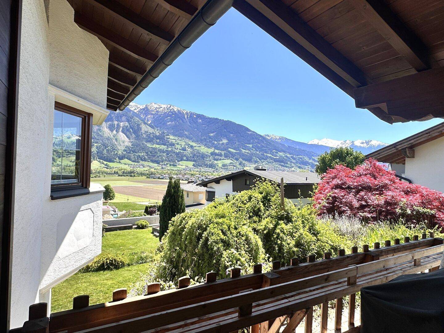 Balkon mit weitem Blick über grüne Hügel, umliegende Häuser und die majestätische Berglandschaft.