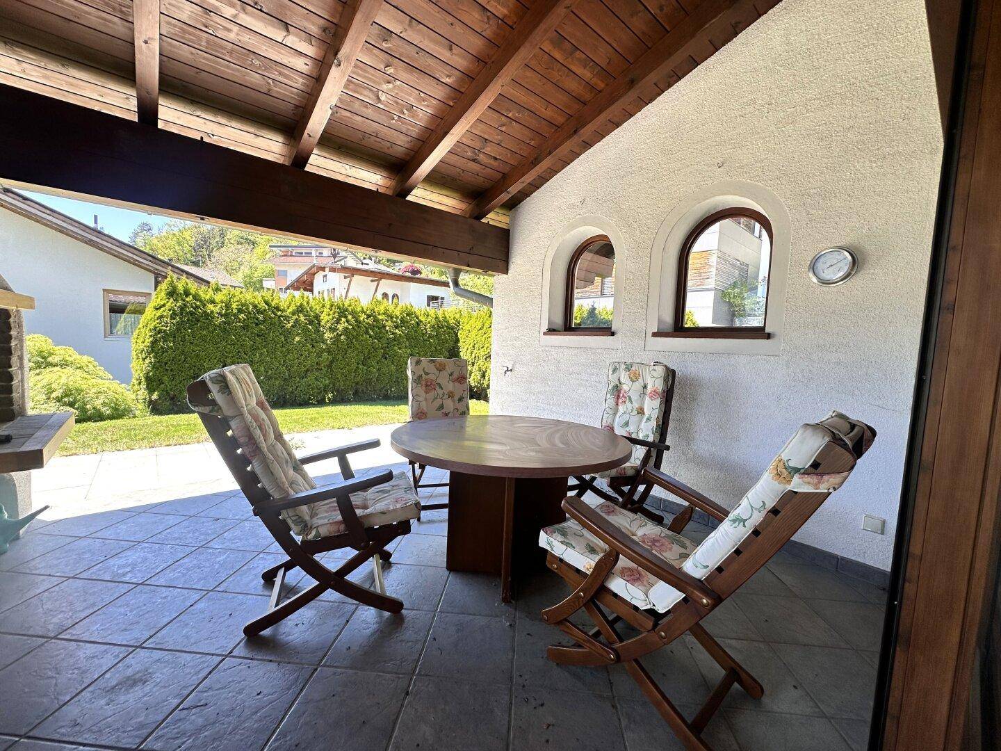 Überdachte Terrasse mit Fliesenboden, Holzdecke und bequemen Gartenmöbeln für entspannte Stunden.