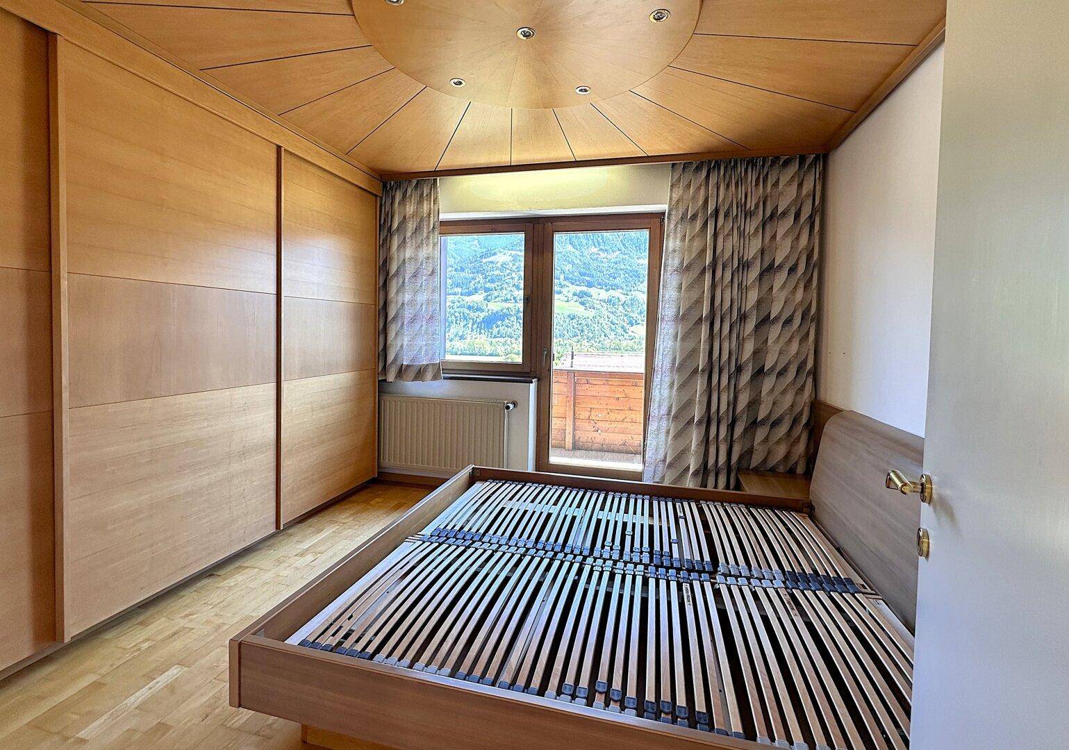Gemütliches Schlafzimmer mit Holzvertäfelung, Parkettboden und Zugang zu einem Balkon mit Bergblick.