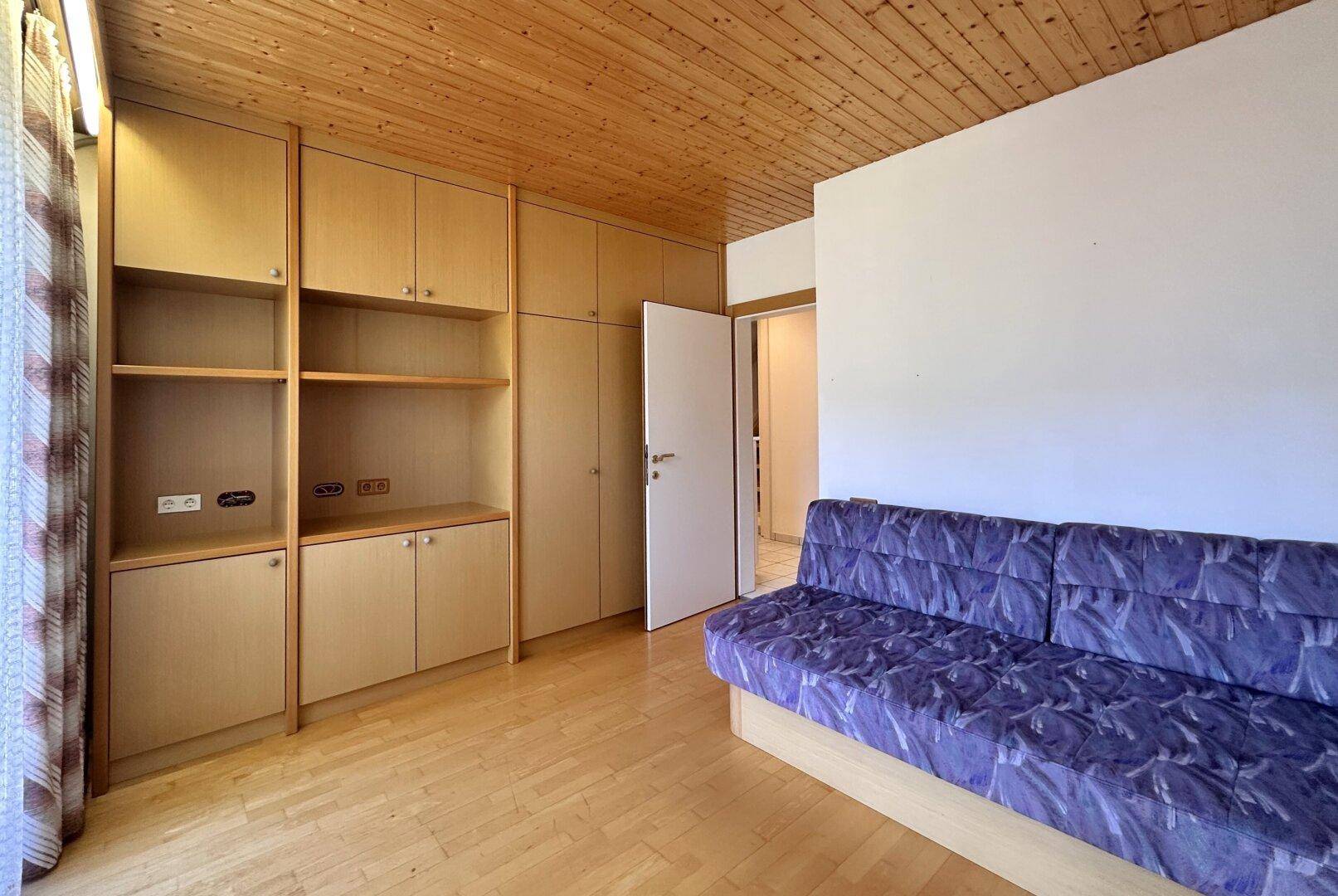 Schlafzimmer mit Parkettboden, Holzdecke und integrierten Regalen und Schränken für Stauraum.