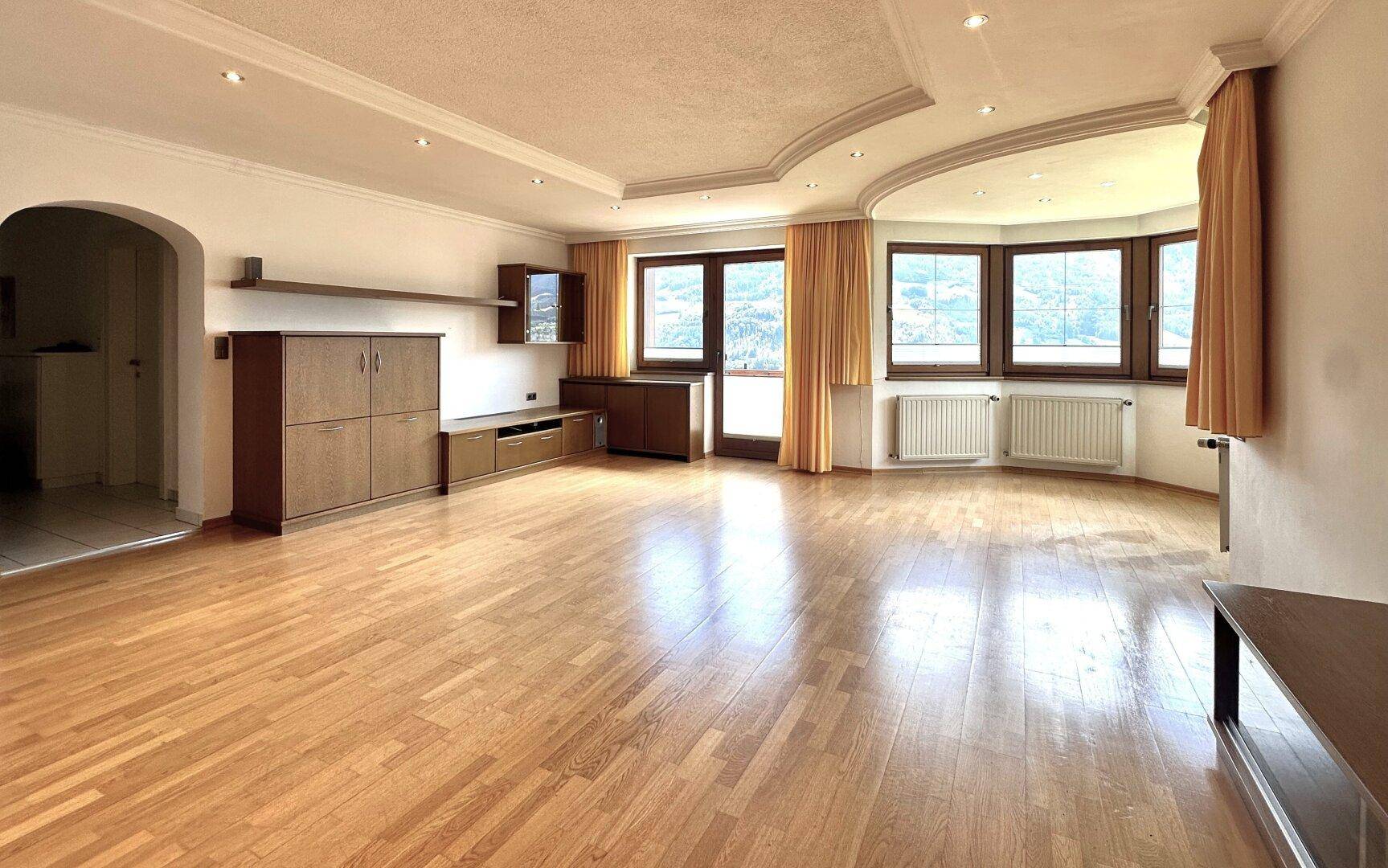 Helles Wohnzimmer mit Parkettboden, Erkerfenstern und einer dekorativen Decke.