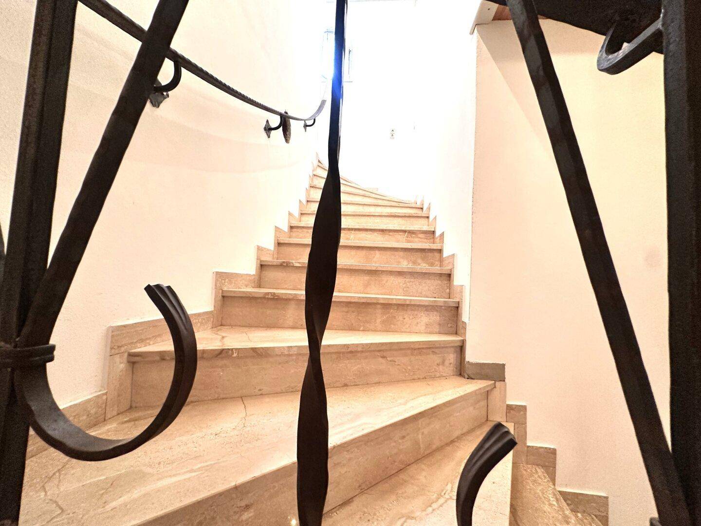 Elegante Treppe mit Marmorstufen und schmiedeeisernem Geländer in einem hellen Treppenhaus.