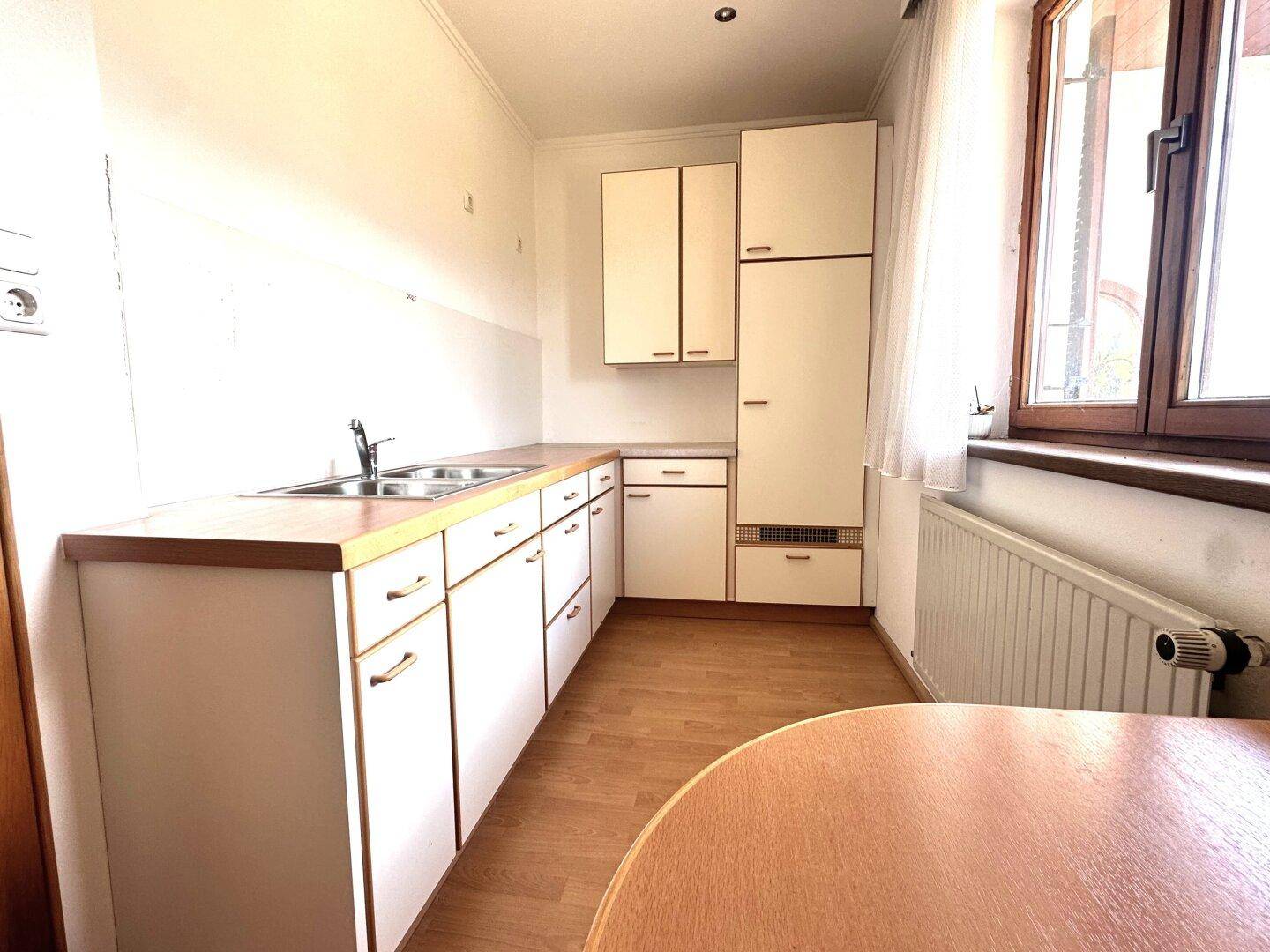 Funktionale Küche mit weißen Schränken, Holzarbeitsplatte, Esstisch und Fenster.