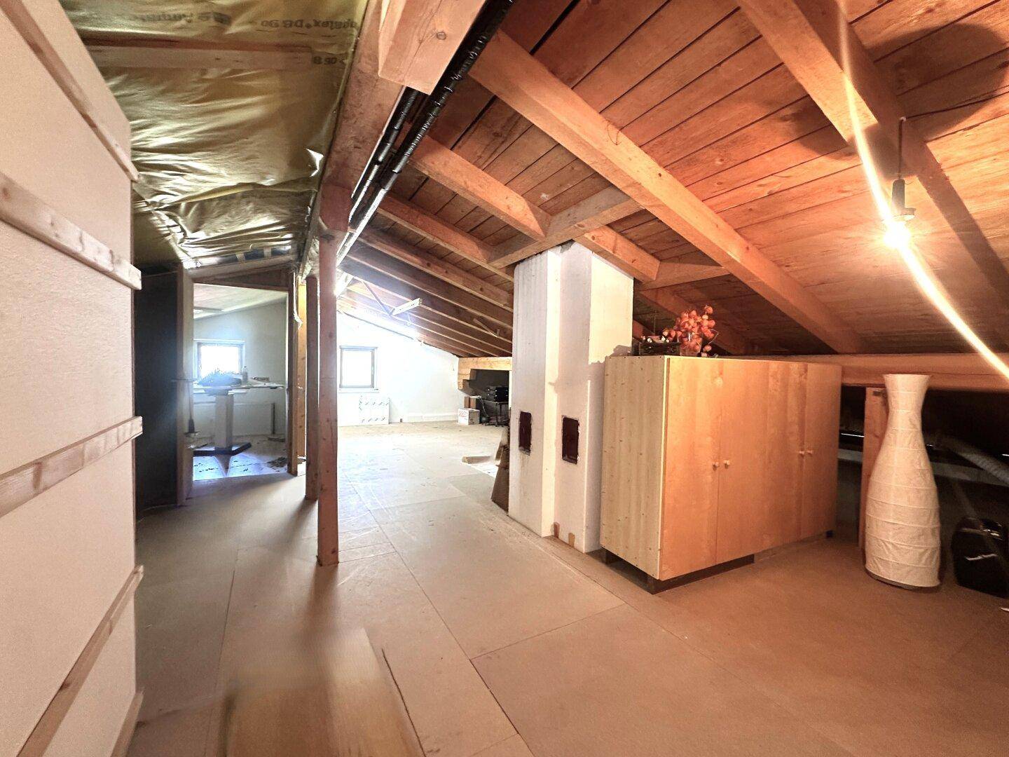 Ausbaufähiger Dachboden mit sichtbaren Holzbalken, Dachschrägen und einem traditionellen Kachelofen.