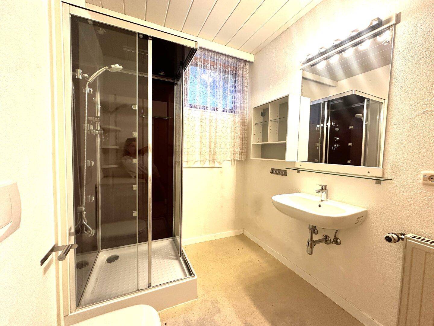 Badezimmer mit Duschkabine, Einzelwaschbecken, Spiegelschrank und Heizkörper.