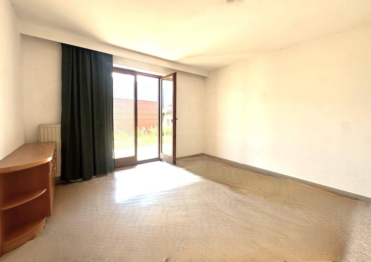 Helles Zimmer mit Teppichboden und einer Glastür, die direkten Zugang zum Garten bietet.