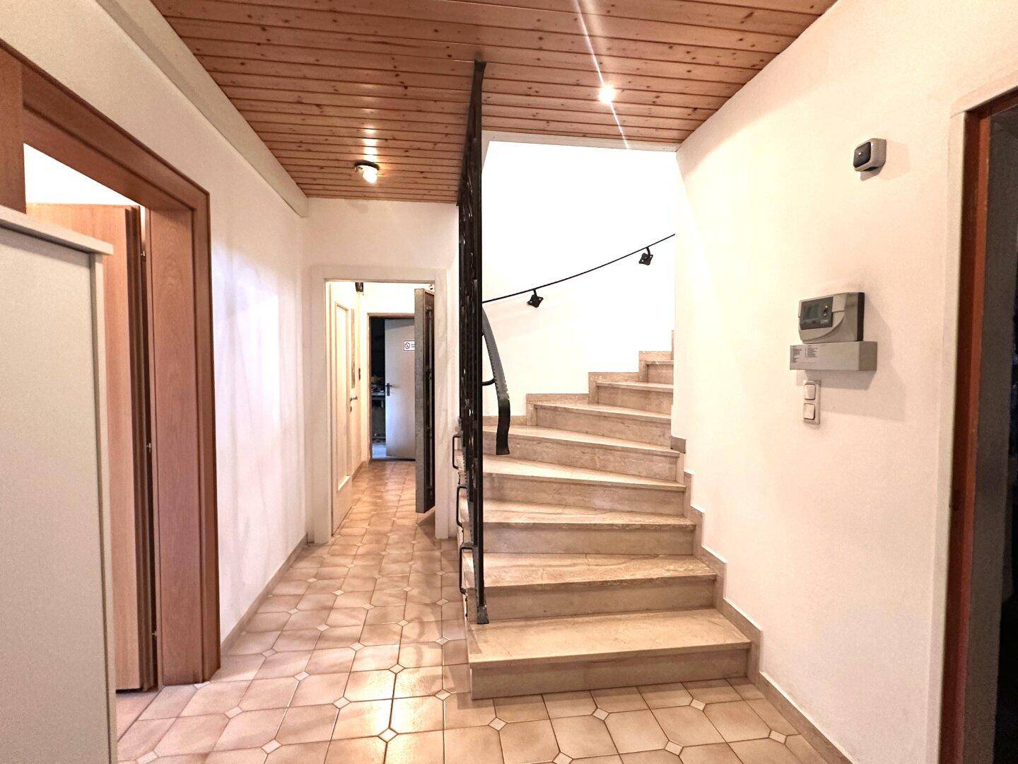 Heller Flur mit Fliesenboden und einer Marmortreppe, die zu den oberen Etagen führt.