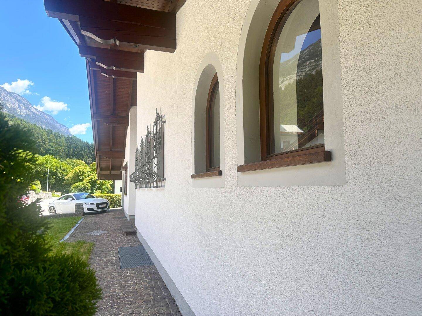 Traditionelle Hausfassade mit Rundbogenfenstern und Blick auf die umliegende Berglandschaft.
