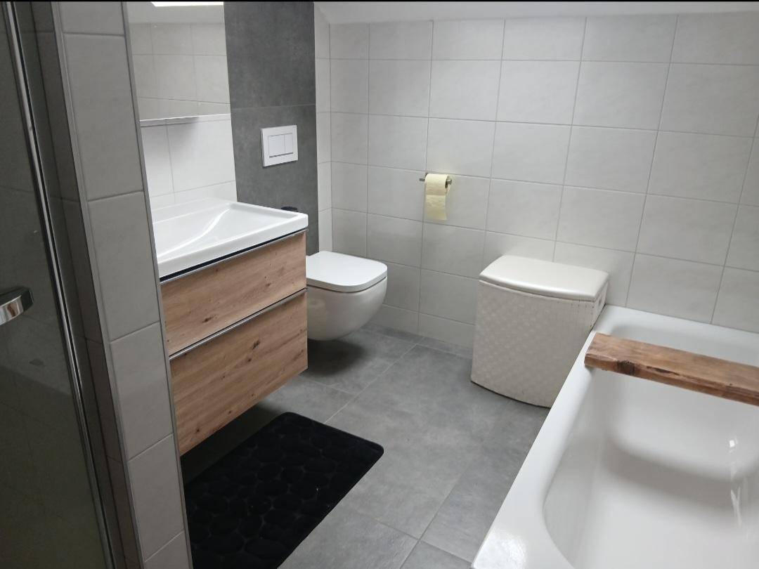 Modernes Badezimmer mit Badewanne, Wand-WC und Holzwaschtischunterschrank.