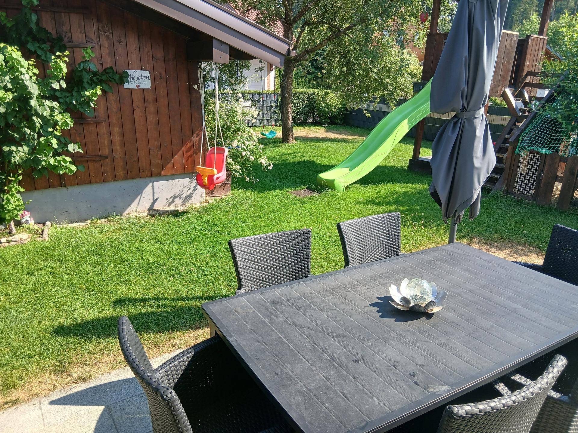 Sonnige Gartenterrasse mit Esstisch, Spielplatz und viel Grünfläche.
