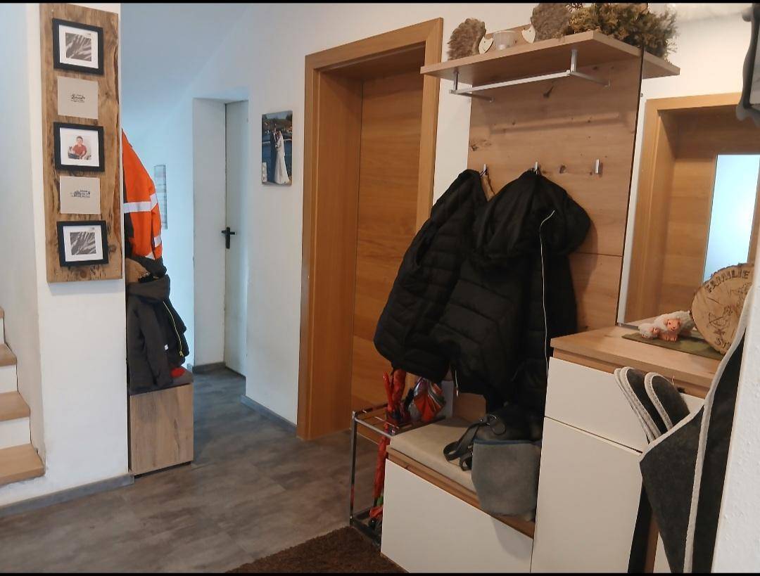 Heller Eingangsbereich mit Holzmöbeln, Garderobe und Treppenzugang.
