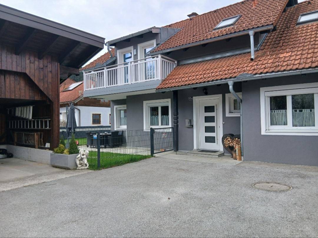 Graues Wohnhaus mit Balkon, Vorgarten und gepflasterter Einfahrt.