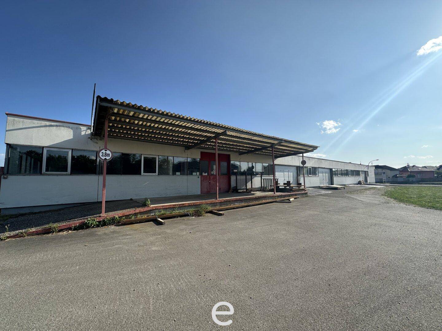 Überdachter Eingangsbereich des Gewerbegebäudes mit einer Höhenbegrenzung von 3,8 Metern und gepflastertem Vorplatz.
