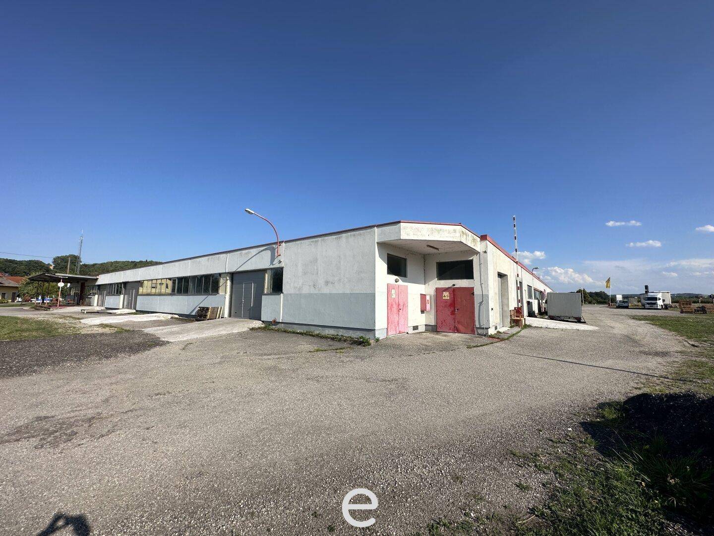 Gewerbegebäude mit sichtbaren Gebrauchsspuren und einem weitläufigen Vorplatz unter klarem Himmel.