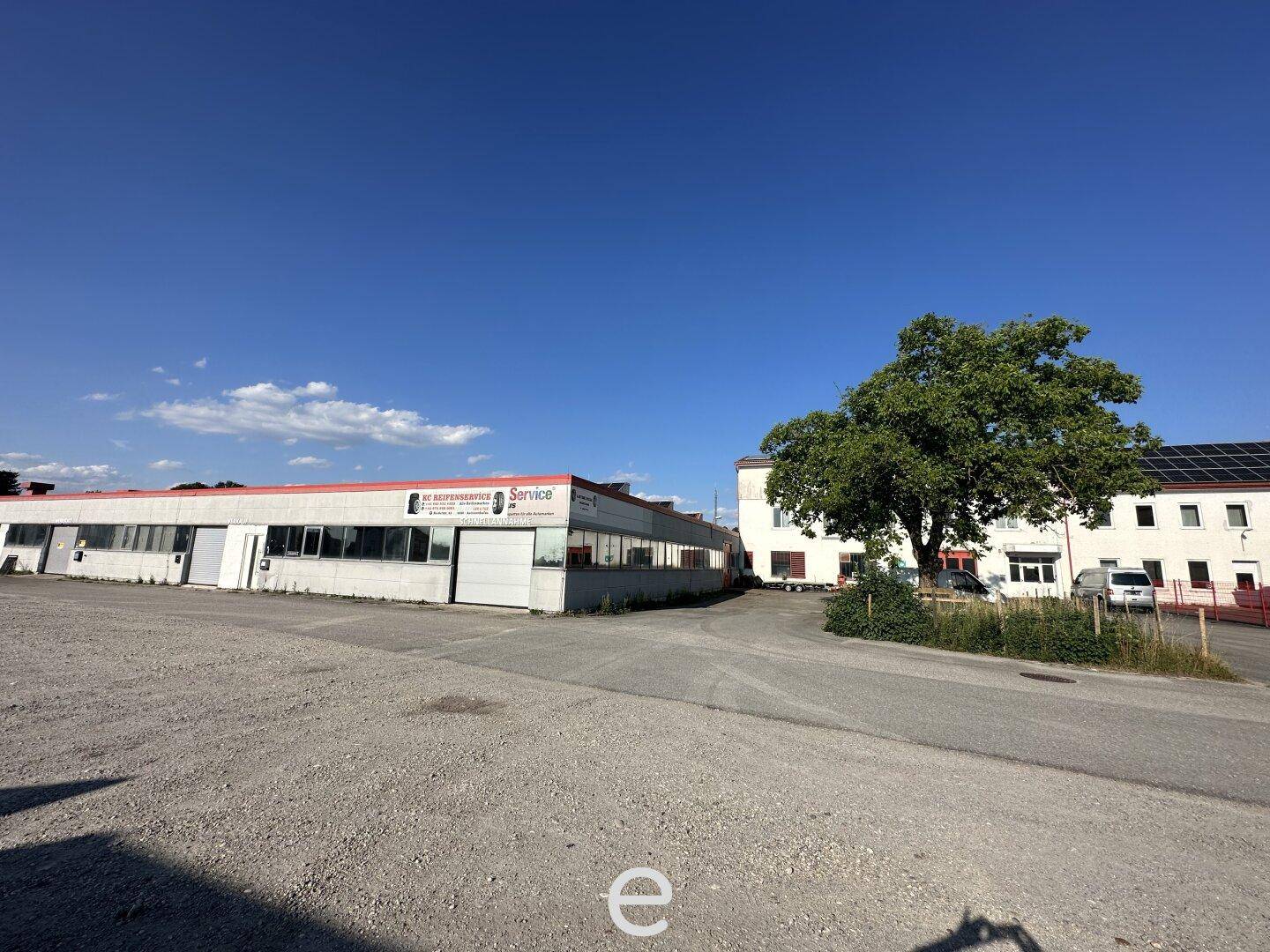 Gesamtansicht des Gewerbekomplexes mit weitläufigem Schotterparkplatz und angrenzendem Gebäude mit Solaranlage.
