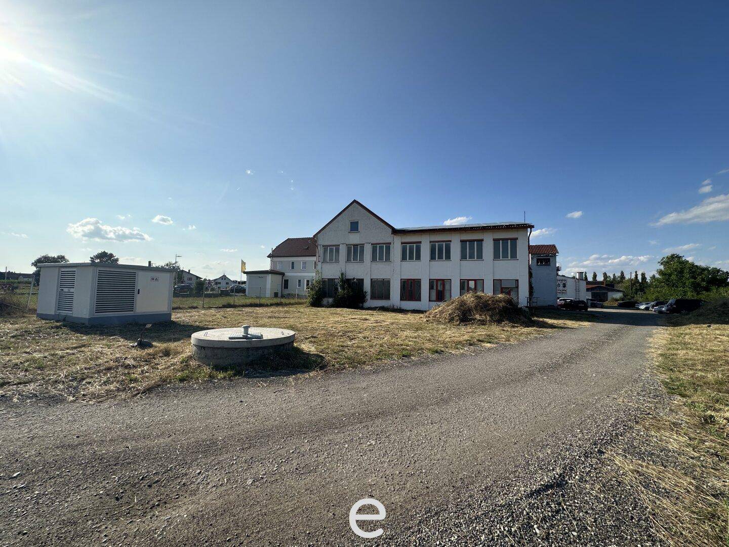 Gebäudeansicht mit Nebengebäuden, einem Schotterweg und weitem Blick in die Landschaft, inklusive Solaranlage.