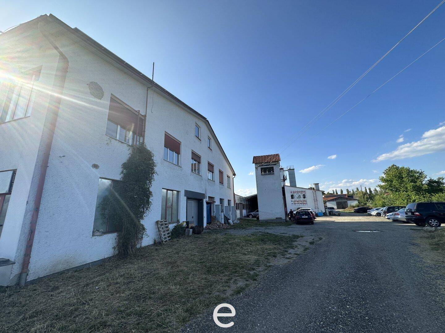 Seitenansicht des Hauptgebäudes mit einem angrenzenden Turm und einem Parkplatz im Hintergrund, das Renovierungsbedarf hat.