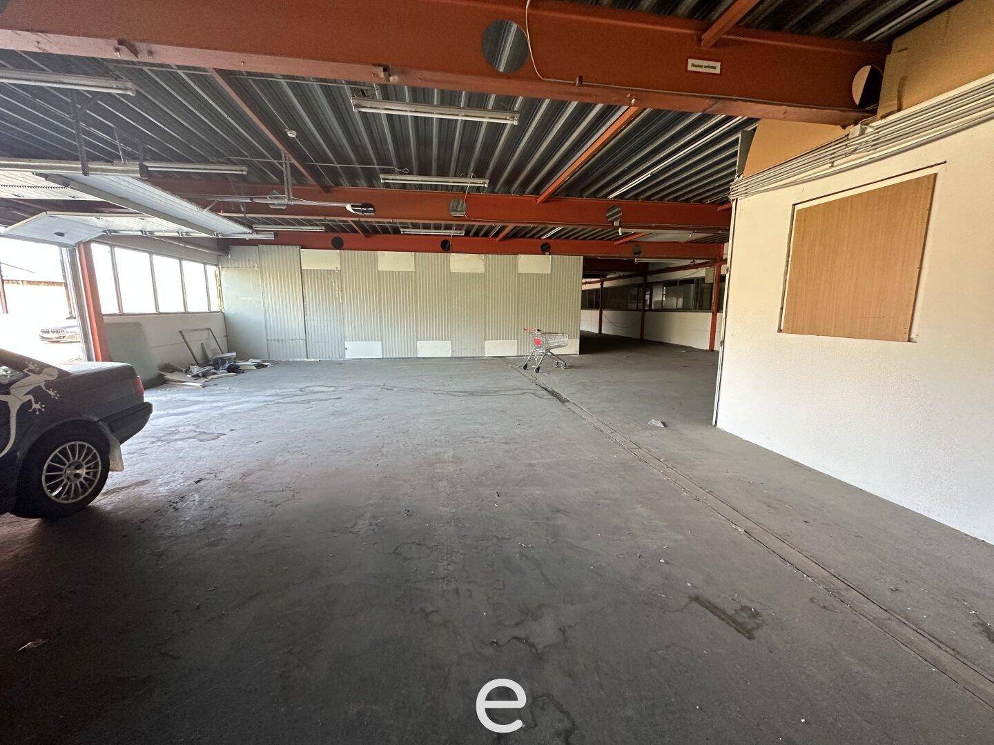 Leere Lagerhalle mit hohen Decken, Betonboden und sichtbaren Stahlträgern, die Renovierungsbedarf zeigt.