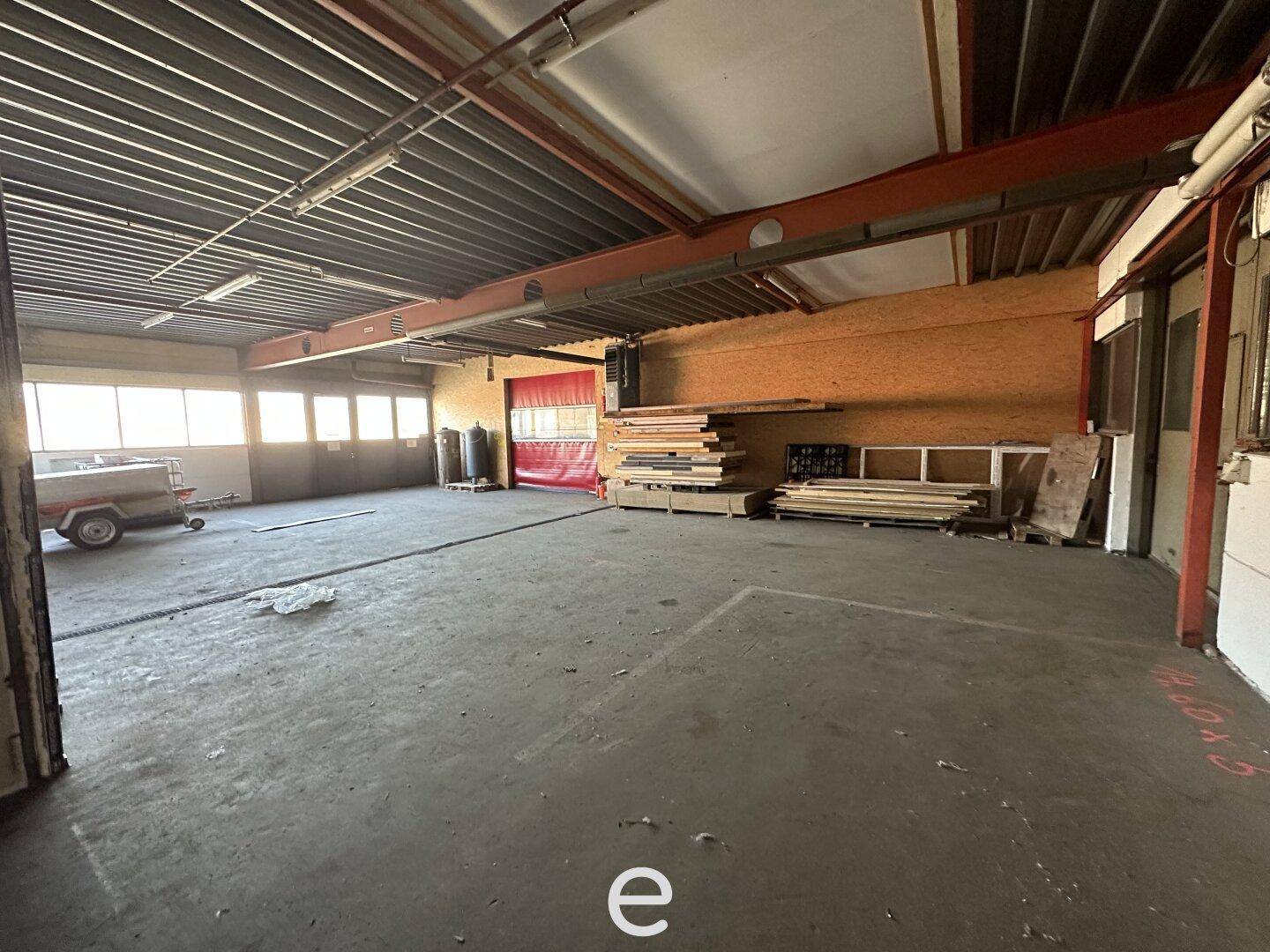 Große Lagerhalle mit Betonboden, sichtbaren Stahlträgern und Materialien an der Wand gelagert, mit Tageslicht.