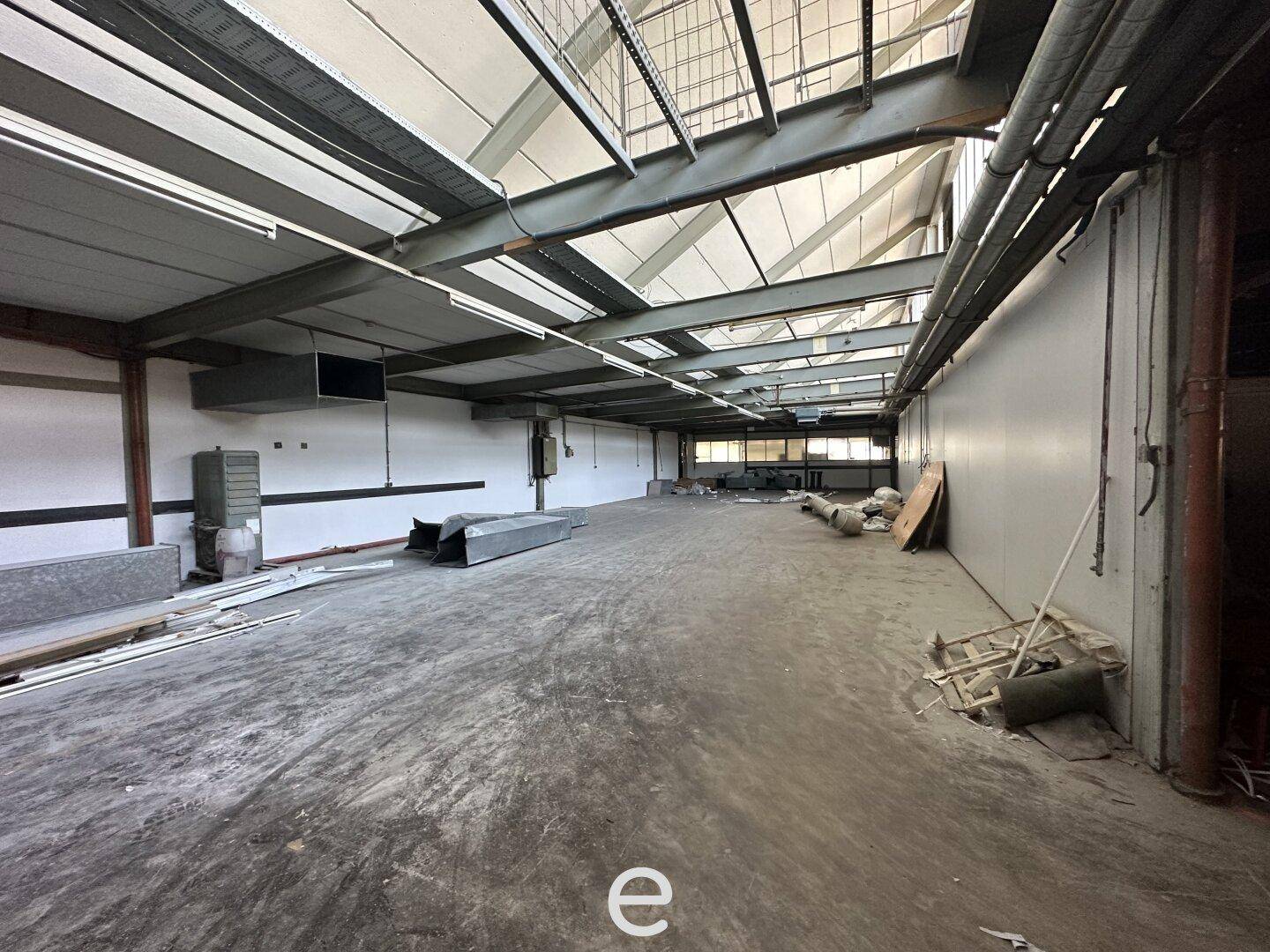 Industrielle Lagerhalle mit sehr hohen Decken, sichtbaren Stahlträgern und Oberlichtern für natürliches Tageslicht.